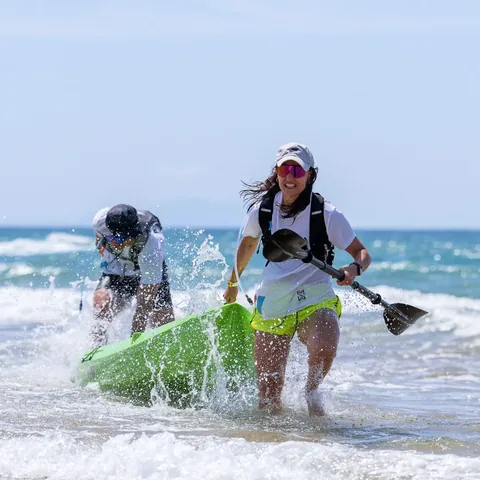 An athlete hauling a kayak through the surf, paddle in hand.